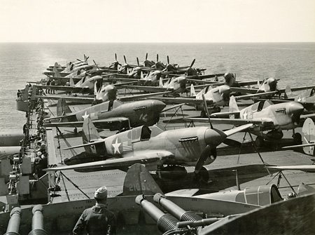Looking aft on USS Ranger flight deck during daily warming up of P-40s. February, 1943